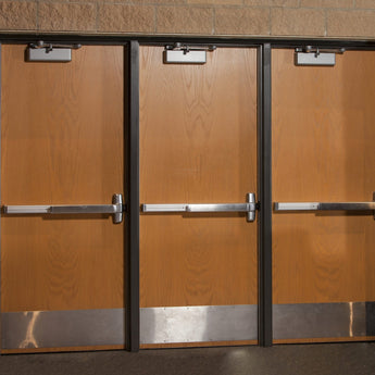 three silver Locks exit devices on brown doors in auditorium