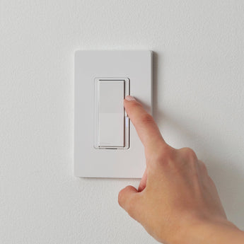 Person turning on white smart light switch with finger on white wall background